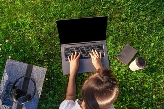 Top view hands on keyboard. Woman working on laptop pc computer with blank black empty screen to copy space in park on green grass sunshine lawn outdoors. Mobile Office. Freelance business concept