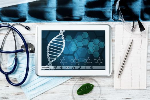 Human genetic research in medical laboratory. Tablet computer with DNA helix structure on screen. Stethoscope, x-ray image and cardiogram on wooden desk. Medical diagnostics and patient genome testing