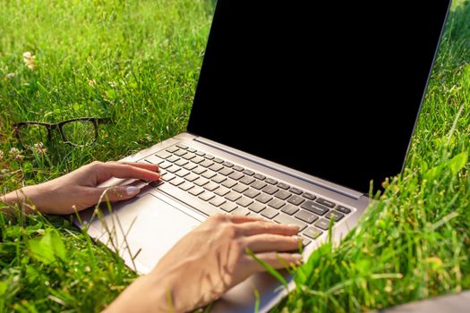 Close up hands on keyboard. Woman working on laptop pc computer with blank black empty screen to copy space in park on green grass sunshine lawn outdoors. Mobile Office. Freelance business concept