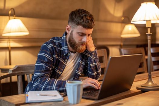 Young professional surfing the Internet on his laptop with cup of coffee on table at coffee shop or home office, working from cafe concept