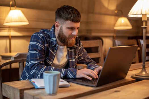 Young professional surfing the Internet on his laptop with cup of coffee on table at coffee shop or home office, working from cafe concept