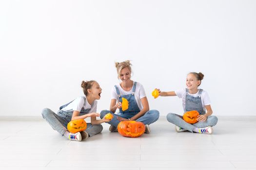 Happy halloween and holidays concept - A mother and her daughters with pumpkins. Happy family preparing for Halloween