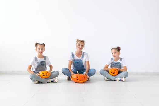 Happy halloween and holidays concept - A mother and her daughters with pumpkins. Happy family preparing for Halloween