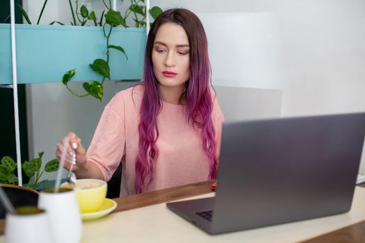 Young woman with pink hair with laptop computer sitting in cafe, intelligent female student working on net-book after her lectures in University