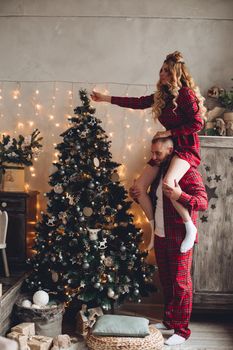 Full length of a couple in red checked pajamas decorating Christmas tree together.