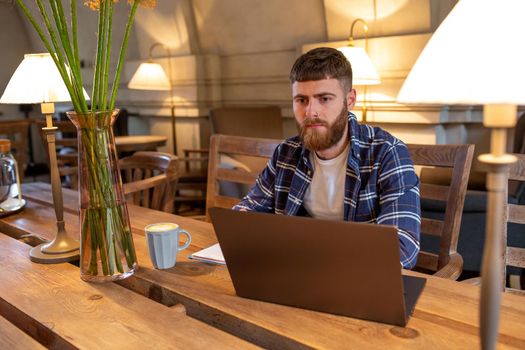 Young professional surfing the Internet on his laptop with cup of coffee on table at coffee shop or home office, working from cafe concept