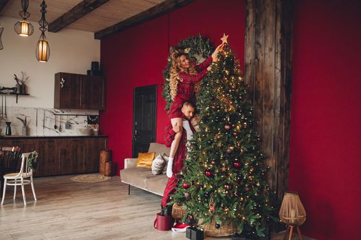 Happy wife and husband in matching clothes helping ornate home together on Christmas eve