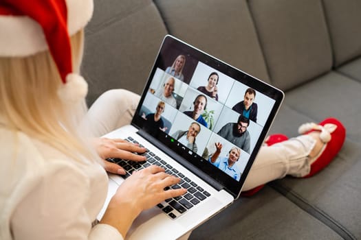 A young smiling woman wearing red Santa Claus hat making video call on social network with family and friends on Christmas day.