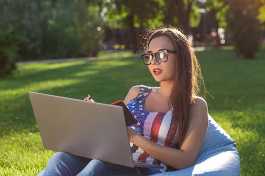 Young cute girl with laptop, sit on bean bag in garden or park, on green grass. Success small business, modern lifestyle, information technology, or online shopping concept