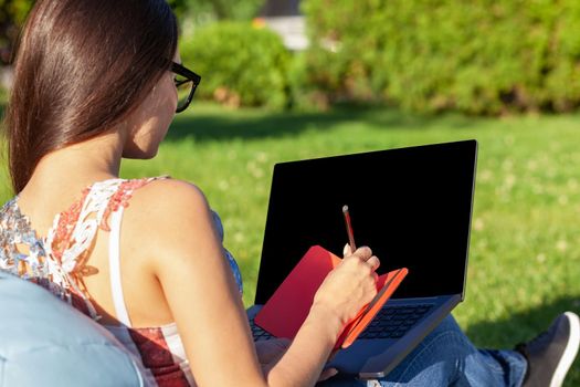 Close up hands on keyboard. Woman working on laptop pc computer with blank black empty screen to copy space in park on green grass sunshine lawn outdoors. Mobile Office. Freelance business concept