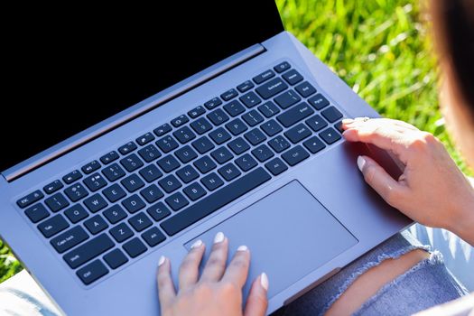 Close up hands on keyboard. Woman working on laptop pc computer with blank black empty screen to copy space in park on green grass sunshine lawn outdoors. Mobile Office. Freelance business concept