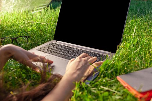 Close up hands on keyboard. Woman working on laptop pc computer with blank black empty screen to copy space in park on green grass sunshine lawn outdoors. Mobile Office. Freelance business concept