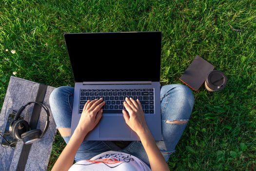 Top view hands on keyboard. Woman working on laptop pc computer with blank black empty screen to copy space in park on green grass sunshine lawn outdoors. Mobile Office. Freelance business concept