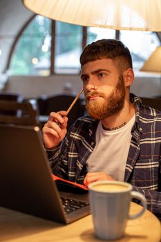 Casual business man or freelancer planning his work on notebook, working on laptop computer with smart phone, cup of coffee on table at coffee shop or home office, working from cafe concept