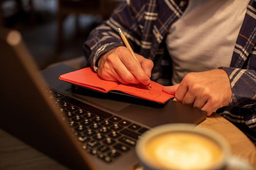 Cropped image of casual business man or freelancer planning his work on notebook, working on laptop computer with smart phone, cup of coffee on table at coffee shop or home office, working from cafe concept