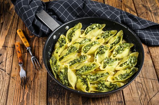 Pasta shells Conchiglioni stuffed with spinach and cheese baked with sauce in a pan. Wooden background. Top view.