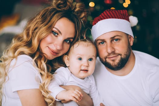 Close up of happy parents hugging their cute baby on Christmas eve. Holiday concept