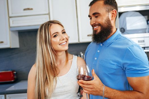 Cheerful smiling couple cooking and drinking wine in kitchen at home