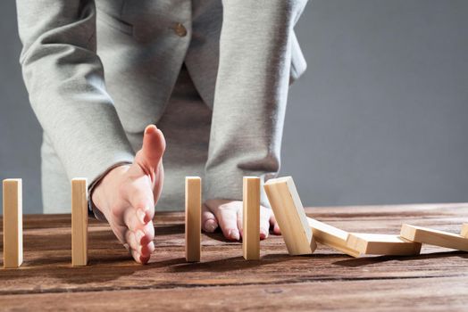 Close up female hand interrupting domino effect. Operative business solution, strategy and successful intervention. Business assistance concept with wooden blocks. Protection from economic crisis.