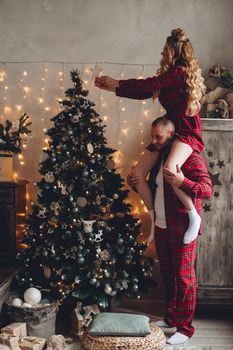 Young man with his girlfriend on his shoulders helping her decorate the Christmas tree