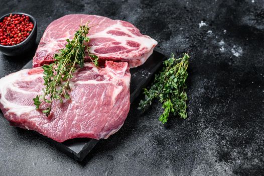 Raw pork meat steaks on a marble board. Black background. Top view. Copy space.