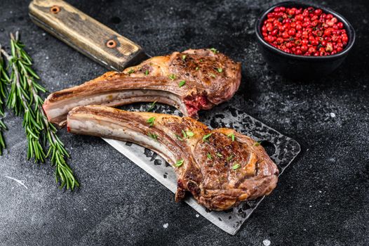 Barbecue grilled lamb chops on a butcher meat cleaver. Black background. Top view.