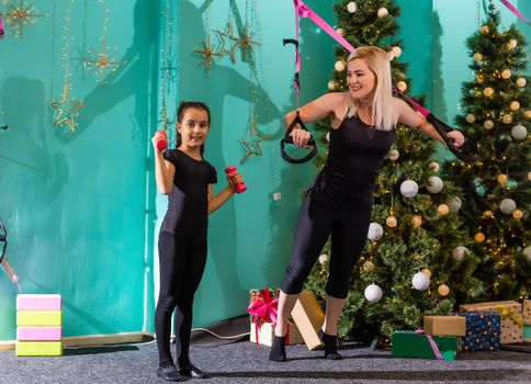 mother and daughter doing fitness near the christmas tree at gym. New Year. Christmas, holidays, fitness, and gym concept.