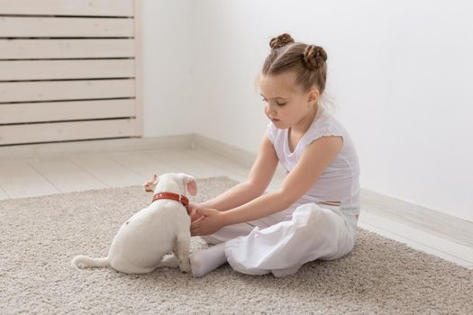 people, children and pets concept - little child girl sitting on the floor with cute puppy and playing.