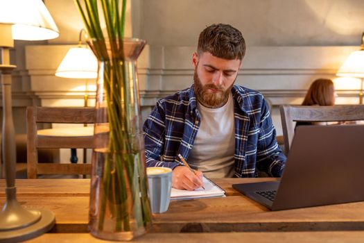 Casual business man or freelancer planning his work on notebook, working on laptop computer with smart phone, cup of coffee on table at coffee shop or home office, working from cafe concept