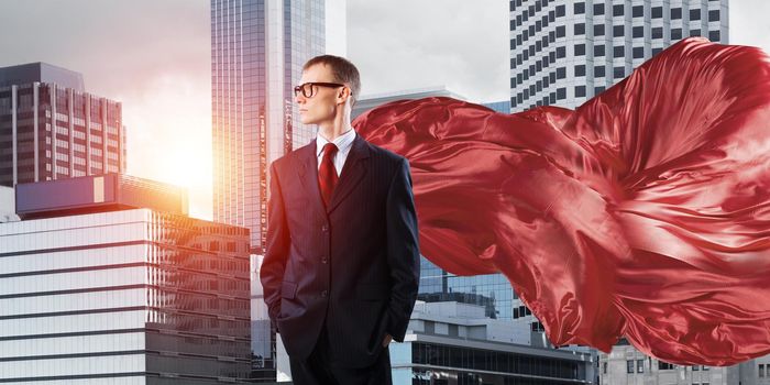 Young confident businessman wearing red cape against modern city background