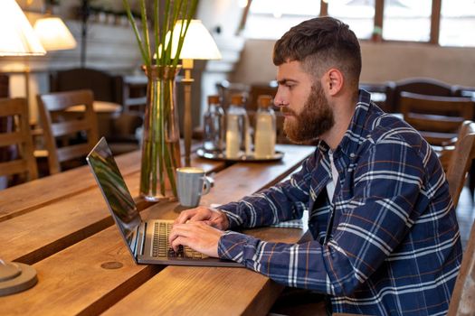 Young professional surfing the Internet on his laptop with cup of coffee on table at coffee shop or home office, working from cafe concept