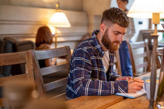 Casual business man or freelancer planning his work on notebook, working on laptop computer with smart phone, cup of coffee on table at coffee shop or home office, working from cafe concept