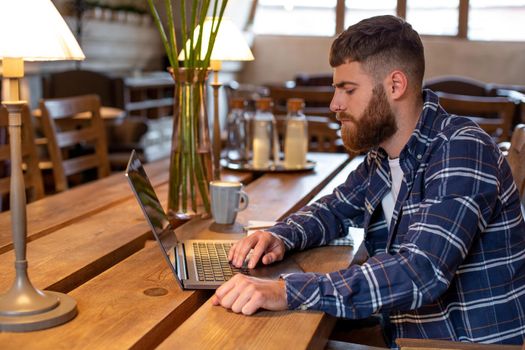 Young professional surfing the Internet on his laptop with cup of coffee on table at coffee shop or home office, working from cafe concept