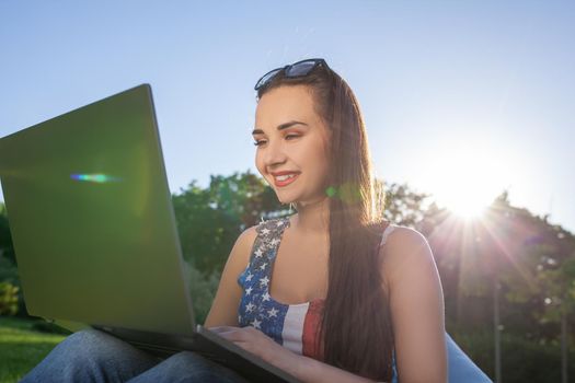 Pretty young woman sitting on bean bag use laptop while resting on grass in park on the sun. Success small business, modern lifestyle, information technology, or online shopping concept