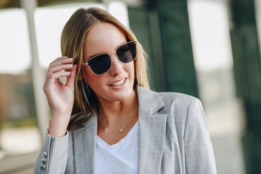 Beautiful young blonde woman with sunglasses in urban background.. Blond girl wearing casual clothes in the street.