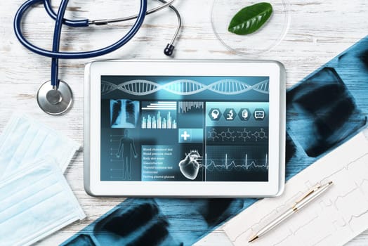 Medical diagnostics in modern hospital. Tablet computer with medical application interface on screen. Top view x-ray images, stethoscope and cardiogram on wooden desk. Digital technology in clinic.