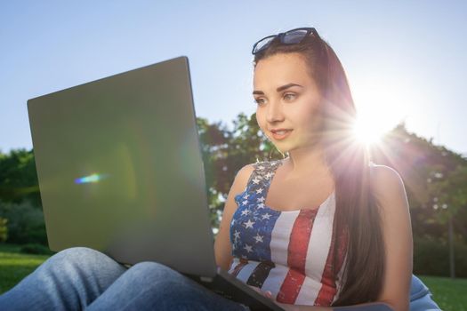 Pretty young woman sitting on bean bag use laptop while resting on grass in park on the sun. Success small business, modern lifestyle, information technology, or online shopping concept