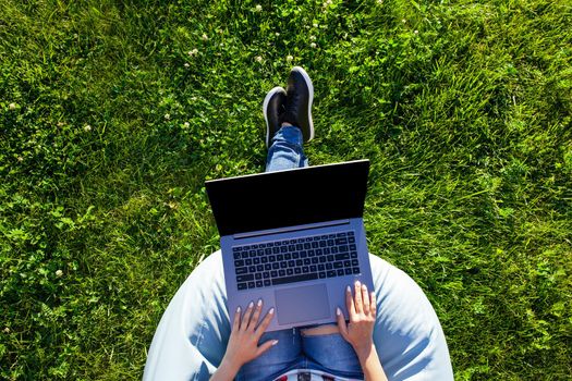 Top view hands on keyboard. Woman working on laptop pc computer with blank black empty screen to copy space in park on green grass sunshine lawn outdoors. Mobile Office. Freelance business concept