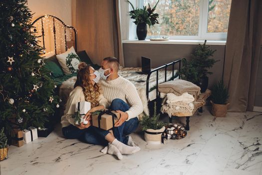 Happy young couple wearing protective masks and holding gift boxes on Christmas eve