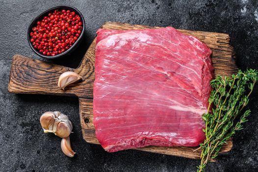 Raw flank or flap beef meat steak on a wooden cutting board. Black background. Top view.