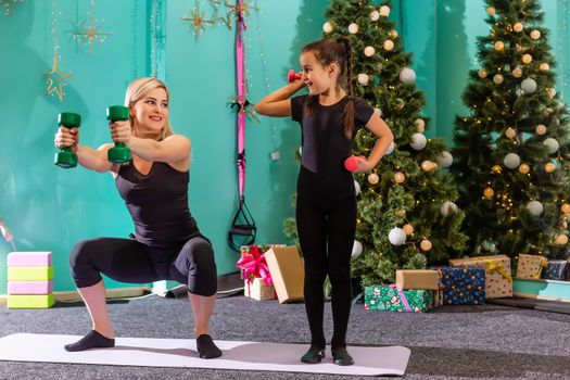 mother and daughter doing fitness near the christmas tree at gym. New Year. Christmas, holidays, fitness, and gym concept.