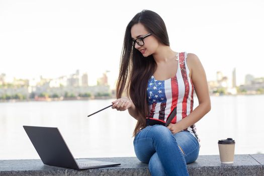 The beautiful young woman sits in the park near river with the laptop. Success small business, modern lifestyle, information technology, or online shopping concept