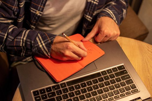 Cropped image of casual business man or freelancer planning his work on notebook, working on laptop computer with smart phone, cup of coffee on table at coffee shop or home office, working from cafe concept
