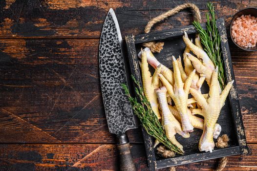 Raw Chicken paws feets on butcher chopping board with knife. Dark wooden background. Top view. Copy space.