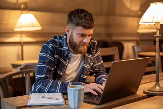 Young professional surfing the Internet on his laptop with cup of coffee on table at coffee shop or home office, working from cafe concept