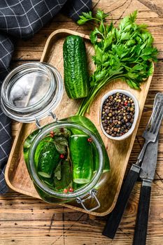 Green salted cucumbers in a glass jar. Wooden background. Top view.