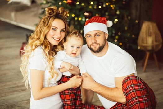 Waist up of smiling couple and cute kid sitting on floor with Christmas tree on the background