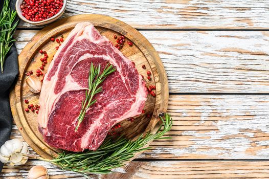 Raw cowboy steak or ribeye on the bone on a cutting board. Marble beef. White wooden background. Top view. Copy space.