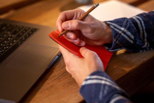 Cropped image of casual business man or freelancer planning his work on notebook, working on laptop computer with smart phone, cup of coffee on table at coffee shop or home office, working from cafe concept