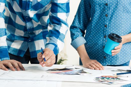 Professional designers discussing architecture project. Creative teamwork and project brainstorming. Close up human hands and construction drawing of building on desk. Industrial engineering company.